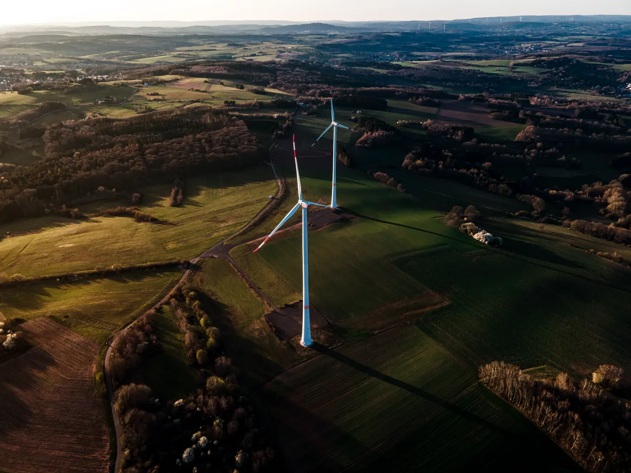 Aerial view of two wind turbines among fields and woodland.