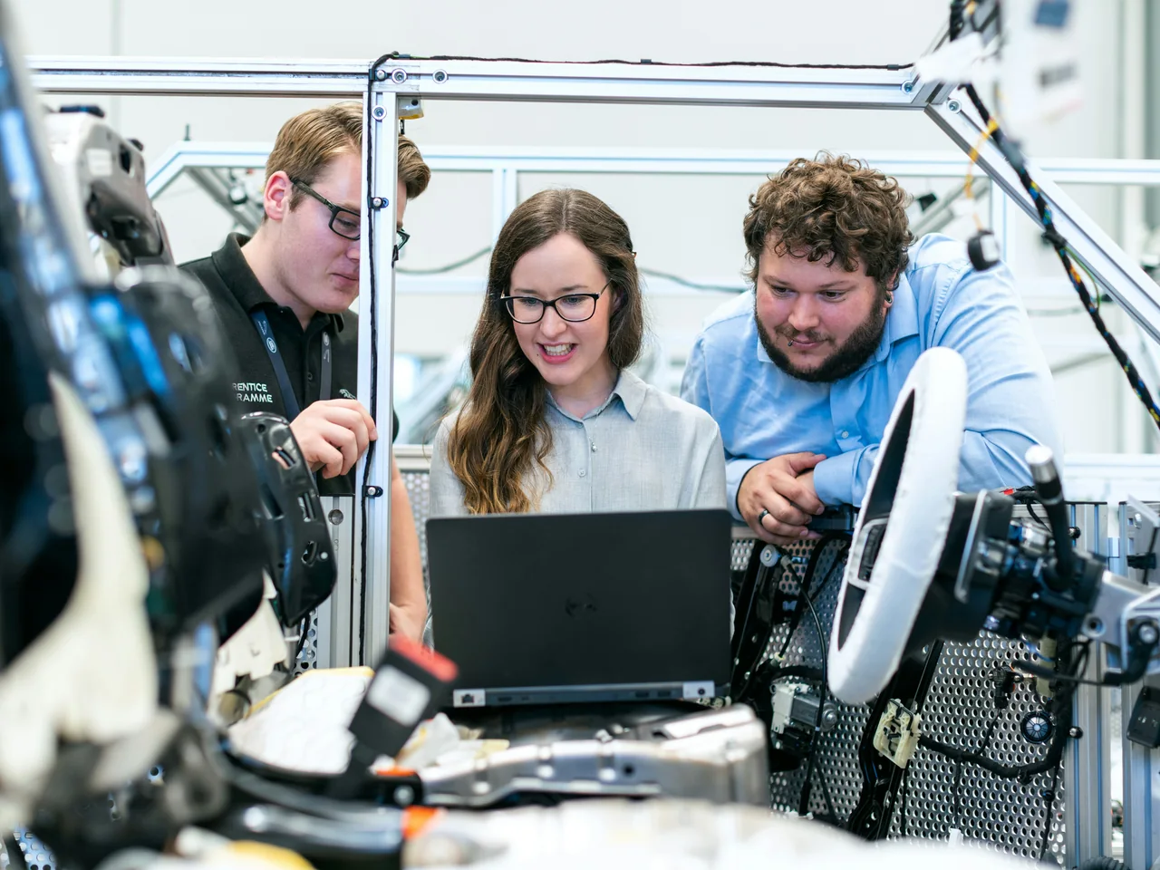 Three engineers working together at a laptop beside an automotive test rig