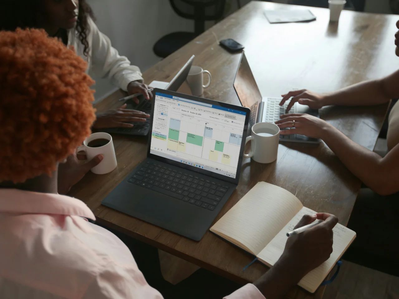 Colleagues discussing a shared calendar on a laptop around a meeting table.