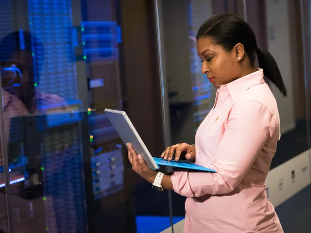 An IT engineer using a laptop beside server racks