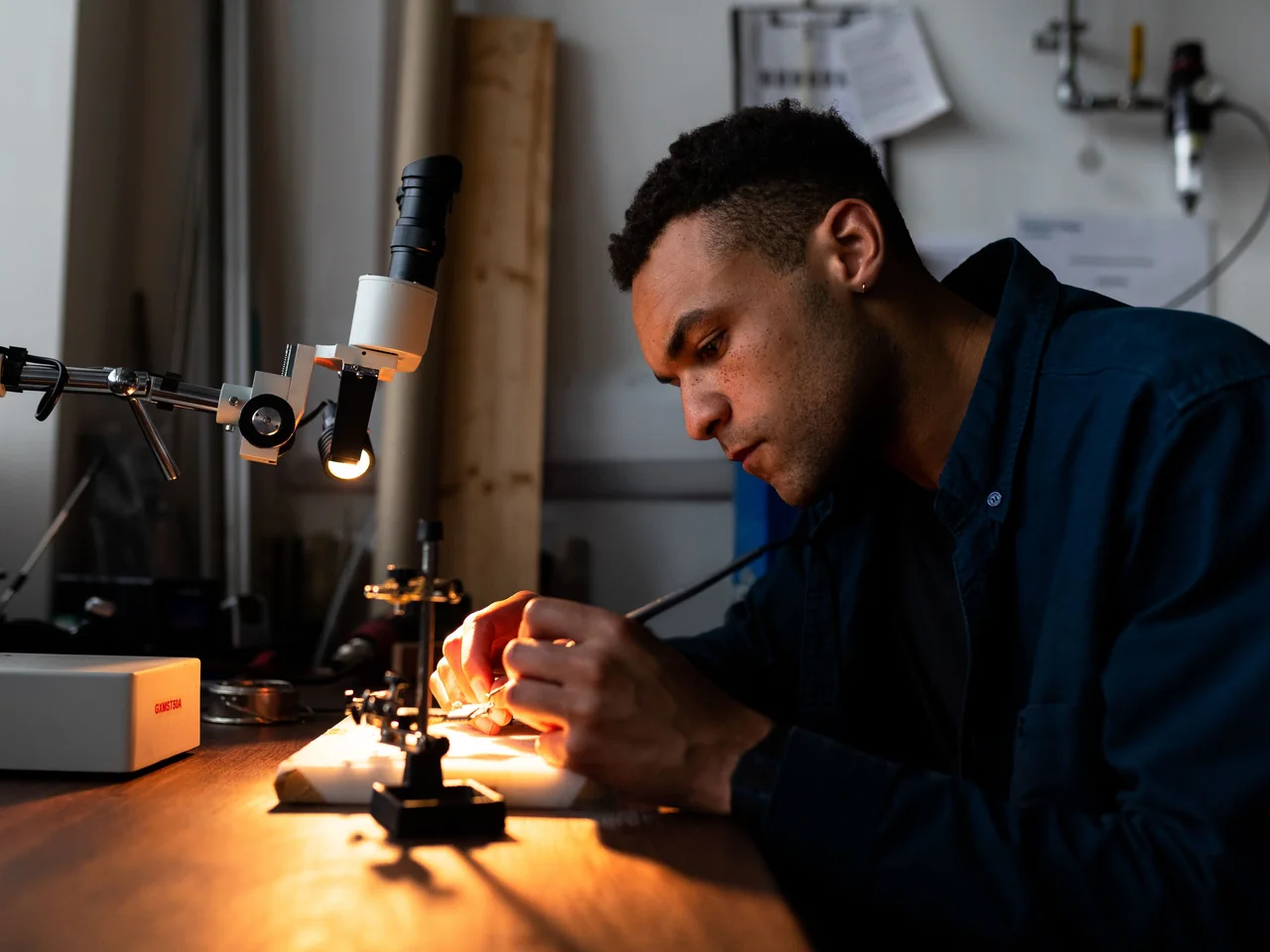 An engineer examining an electronic component at a workshop bench.