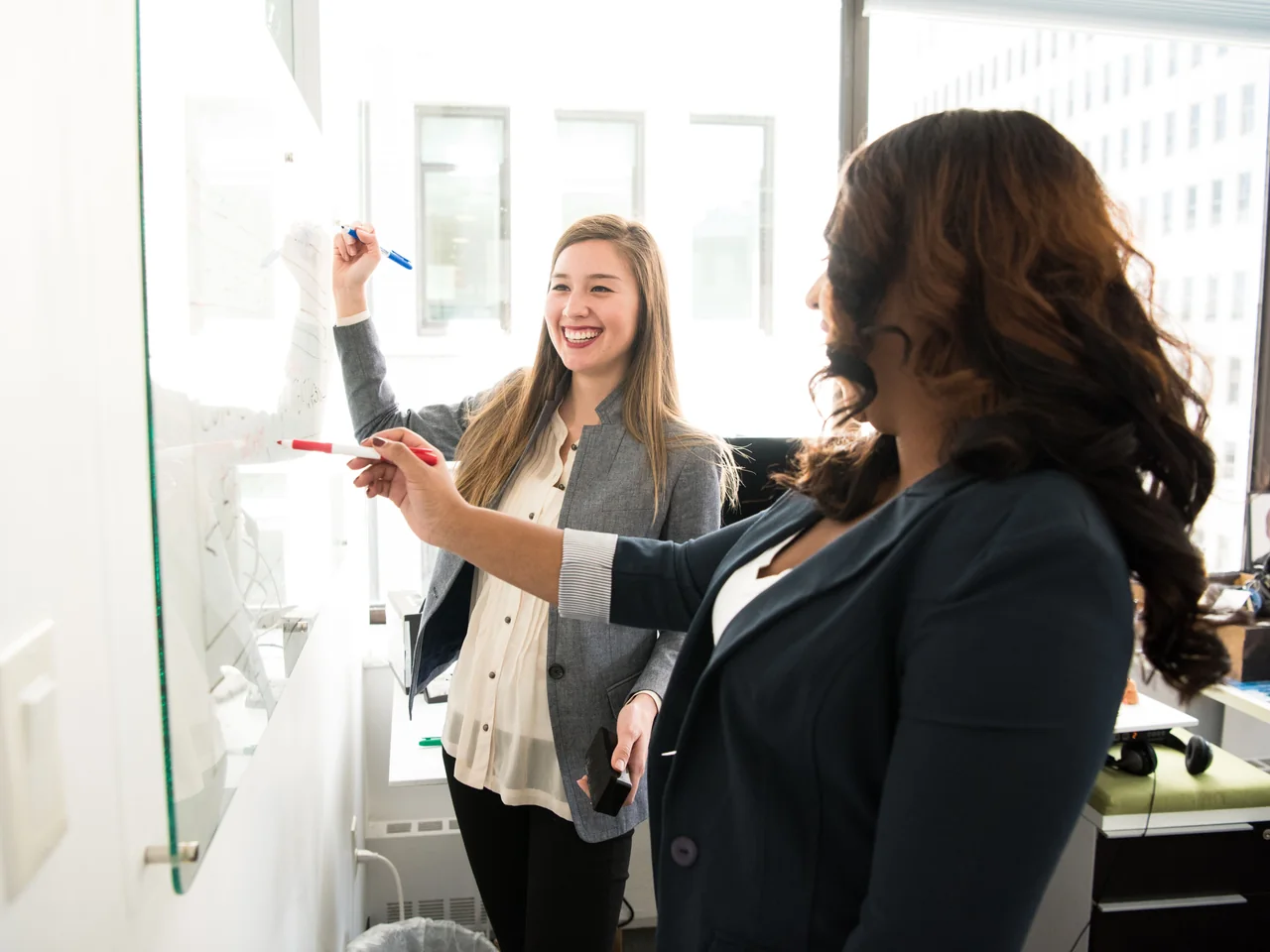 Two colleagues discussing a plan together at a glass whiteboard.
